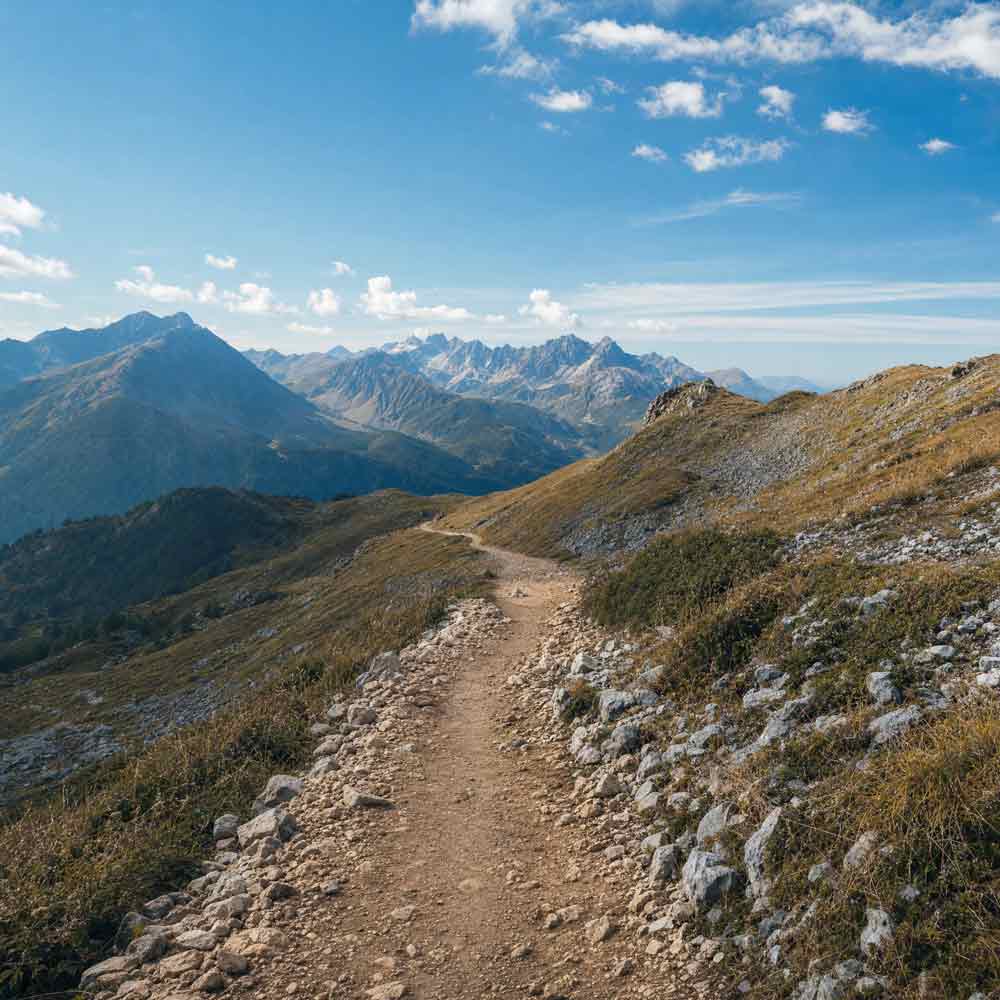 Mountain trail with a view of distant peaks under a blue sky.